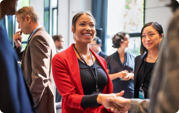 Amex Experiences App - Menschen bei einem Networking-Event, im Vordergrund eine Frau mit Namensschild, die freundlich in die Kamera lächelt.