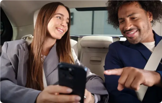 Junge Frau und Mann sitzen im Auto, schauen auf ein Smartphone und lächeln – Bild über der Überschrift ‘Amexcited for Business’.