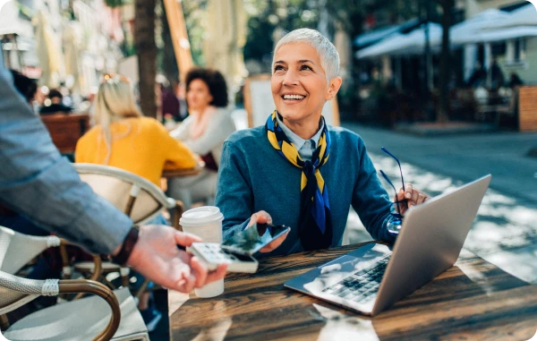 Payment der nächsten Generation - Mann und Frau sitzen im Café mit Laptop, Frau zeigt lachend auf den Bildschirm.