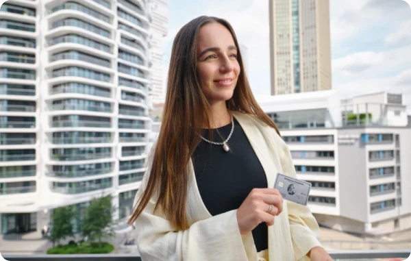 Deine Punkte, deine Entscheidung - Frau steht draußen vor modernen Hochhäusern und lächelt mit Karte und Handy in der Hand.