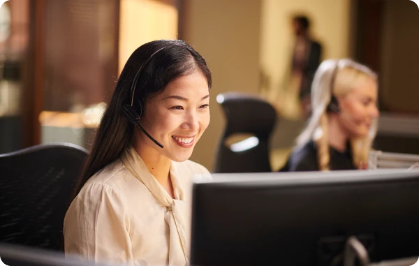 GlobalAssist® – Notfallhilfe im Ausland - Lächelnde Frau mit Headset in einem Callcenter spricht mit einem Kunden.