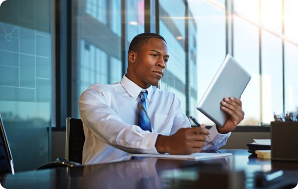 Privathaftpflicht- & Prozesskosten-Versicherung - Mann im Anzug telefoniert im Büro mit Blick auf Dokumente und Laptop.
