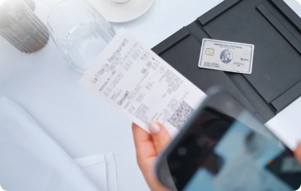 Unbegrenzt punkten - Hand hält eine Quittung über einem Tisch mit einer American Express Karte und Smartphone im Vordergrund.