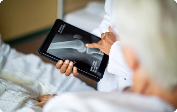 Reise-Unfallversicherung - Frau liegt im Hotelbett und liest ein Tablet.