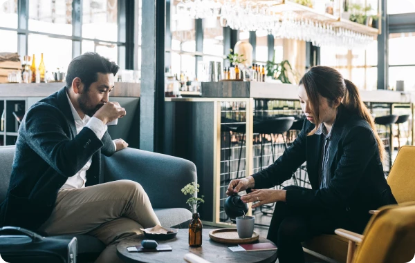 Reisekomfort-Versicherung - Geschäftsleute unterhalten sich in einer Flughafenlounge bei Getränken.