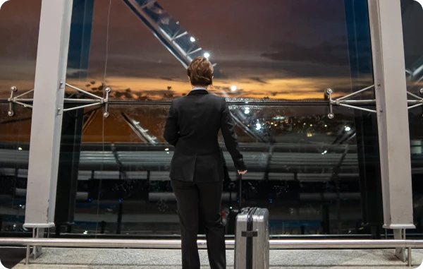 Reiserücktritts- & Reiseabbruchversicherung - Reisende mit Koffern gehen durch einen Flughafen mit Blick auf ein startendes Flugzeug.