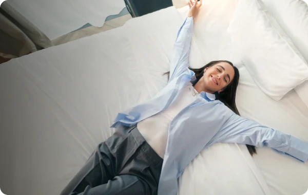 Hotel- und Mietwagen-Statusprogramme - Frau liegt entspannt und lachend quer über einem Hotelbett.