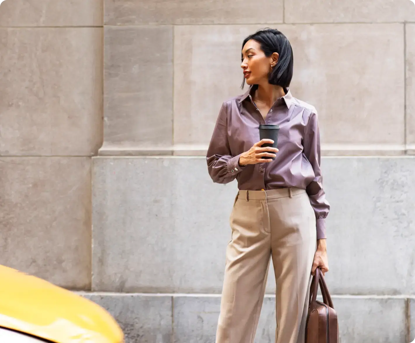 Frau im Business Outfit mit Coffee-to-go vor Steinwand