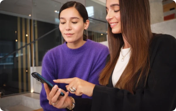 Zwei Frauen betrachten gemeinsam etwas auf einem Smartphone in einem Büro – Bild über der Überschrift ‘Amex Offers’.