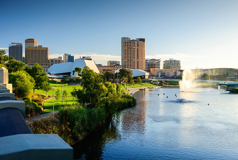 Adelaide city skyline and River Torrens with green parklands and fountains at sunset.