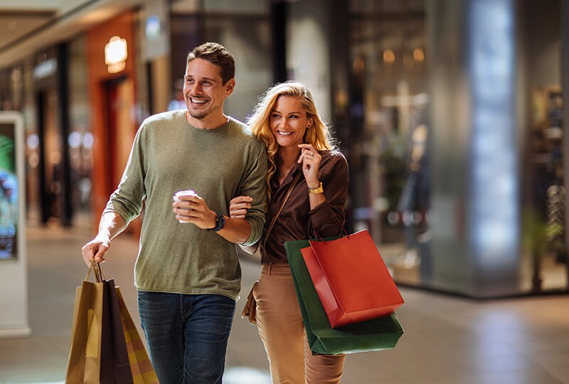 Smiling couple walking through a shopping mall carrying colourful bags.