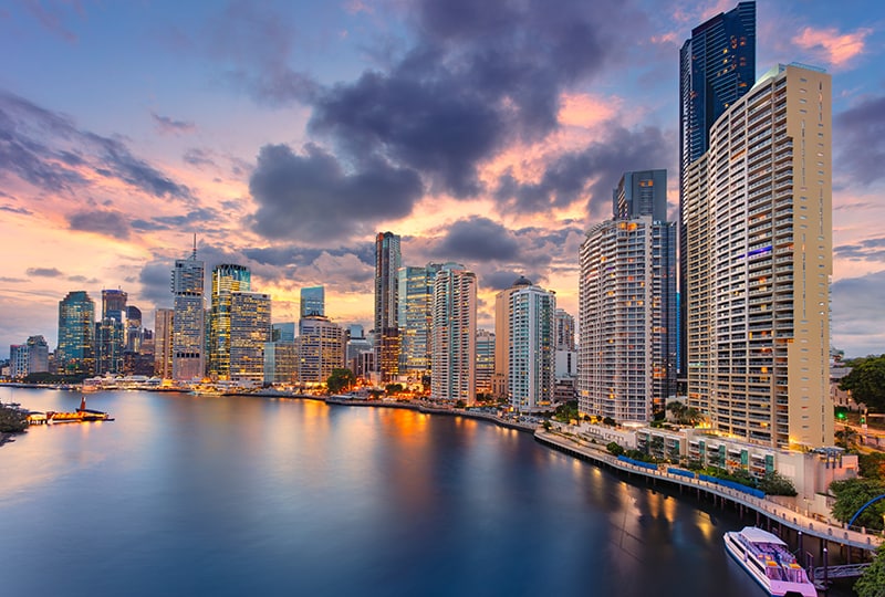 Brisbane city skyline reflecting in the river at sunset with colourful clouds overhead.