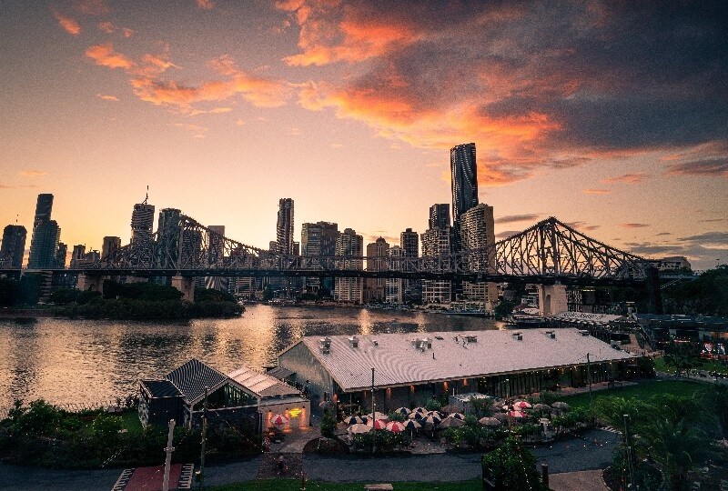  Story Bridge and Brisbane skyline at dusk with glowing clouds and riverside dining below.