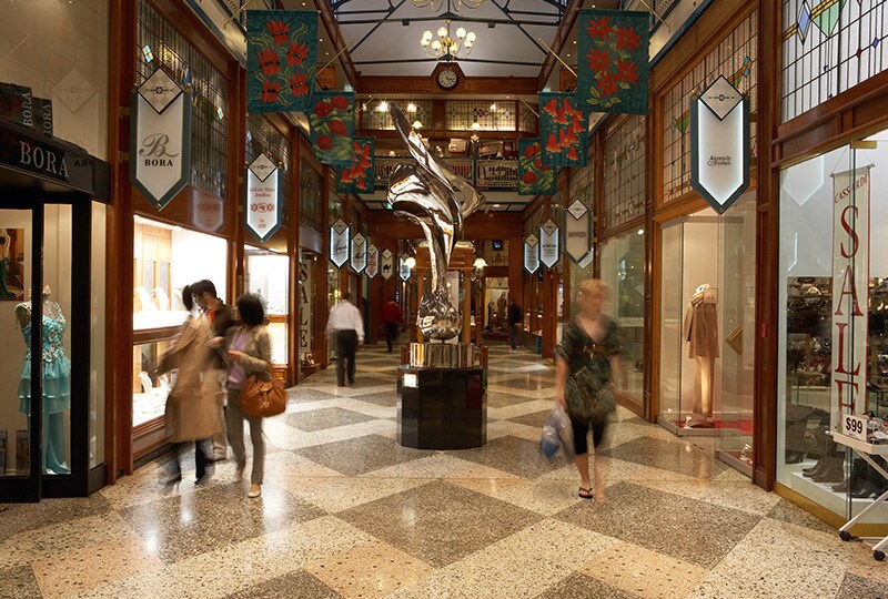 Interior of Brisbane shopping arcade with decorative lighting, boutique stores, and people walking through.