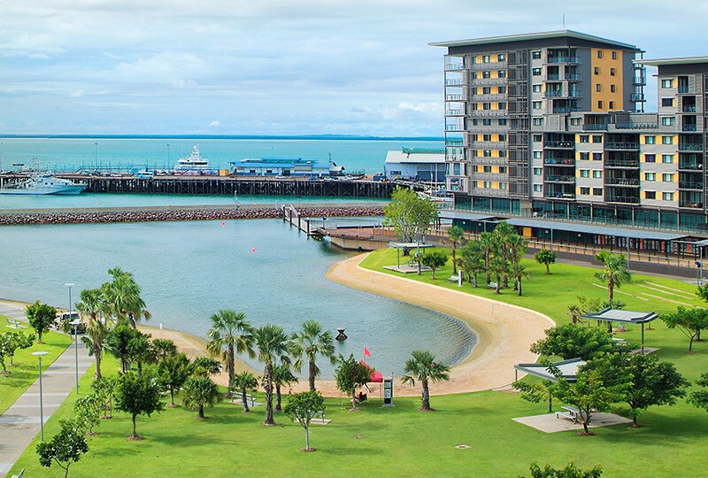 Darwin waterfront with modern apartments, green parklands, and a sandy lagoon beside the harbour.