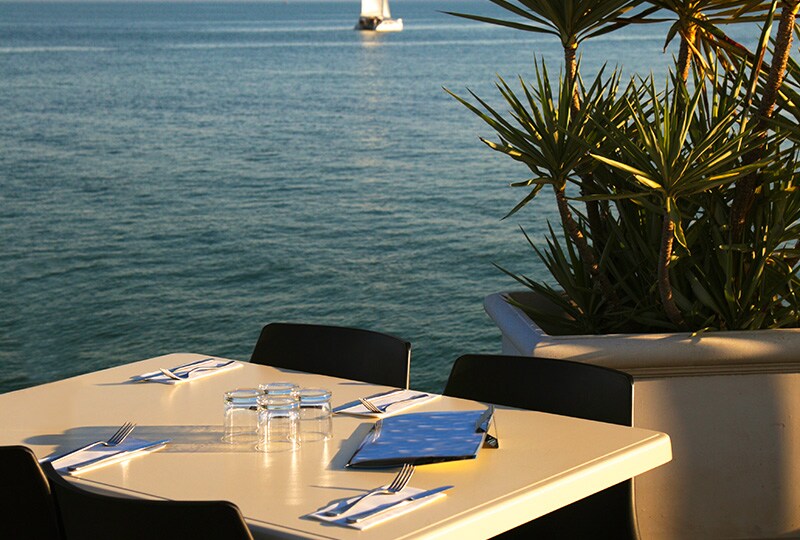 Waterfront restaurant table overlooking the ocean with a sailboat in the distance.