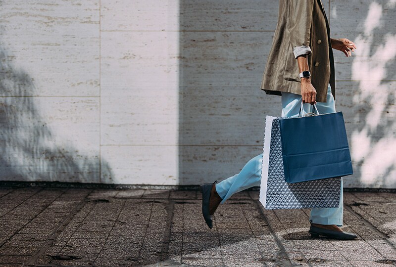Person walking with large shopping bags along a modern urban street.