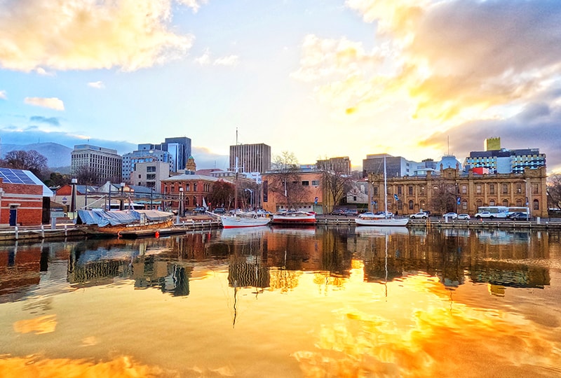 Boats moored at Hobart waterfront reflecting golden sunset light over the city.