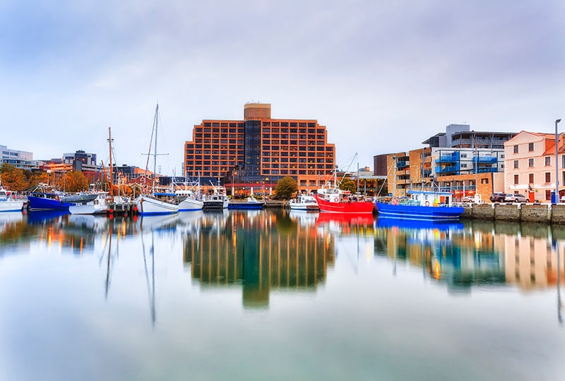 Modern brick hotel building overlooking Hobart marina with colourful fishing boats.