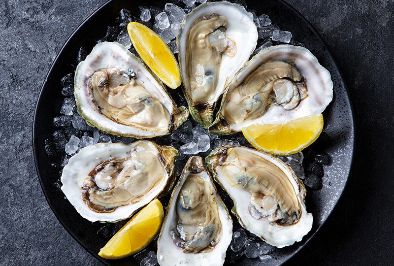 Fresh Tasmanian oysters on a black plate with lemon wedges and crushed ice.