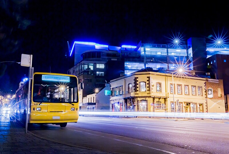Night street scene in Hobart with yellow city bus and illuminated modern buildings.