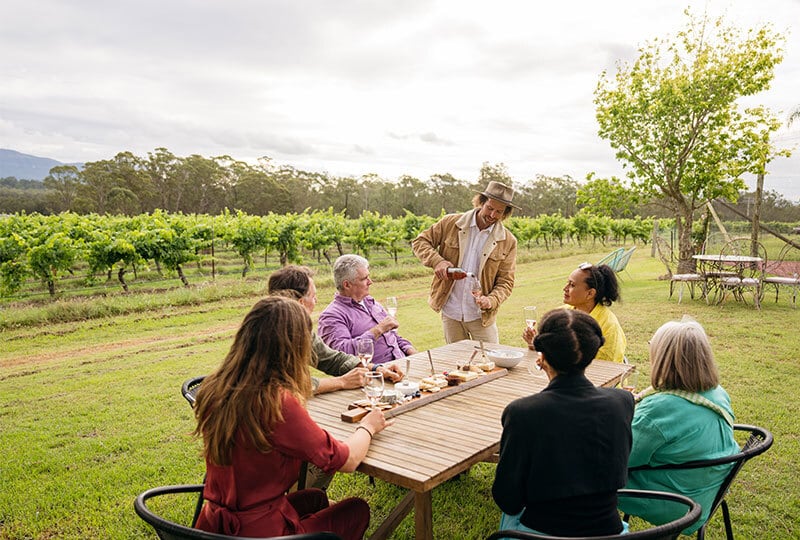 Group enjoying wine tasting and shared food at an outdoor vineyard table in regional Australia.