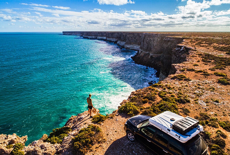 Traveller standing on a cliff edge overlooking turquoise waters along Australia’s rugged coastline.