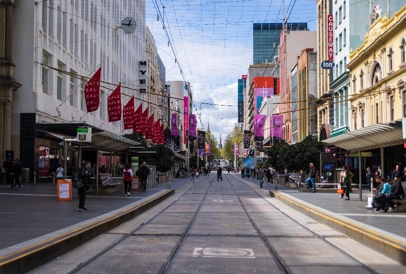 Shoppers walking along Bourke Street Mall with trams and sale banners overhead.