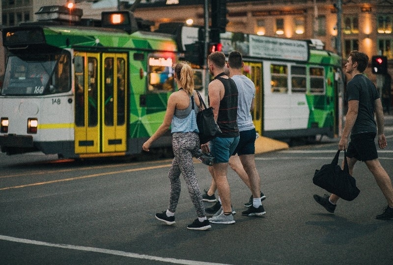 Group of people crossing the street near a green Melbourne tram in the city centre.
