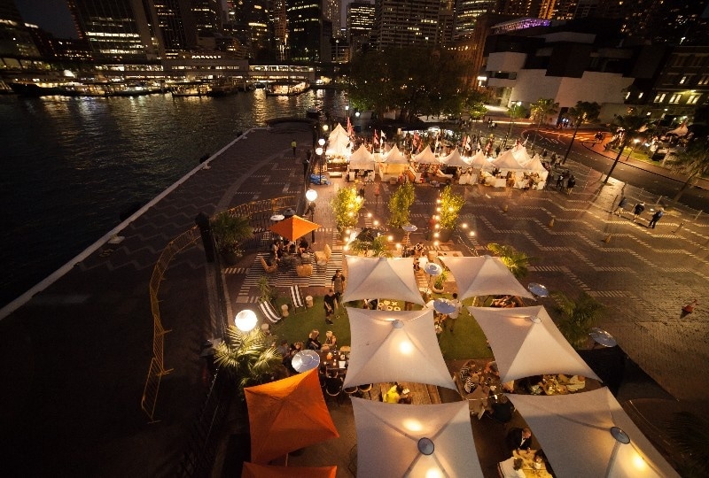 Lively evening dining scene under canopy tents by the waterfront in Sydney.