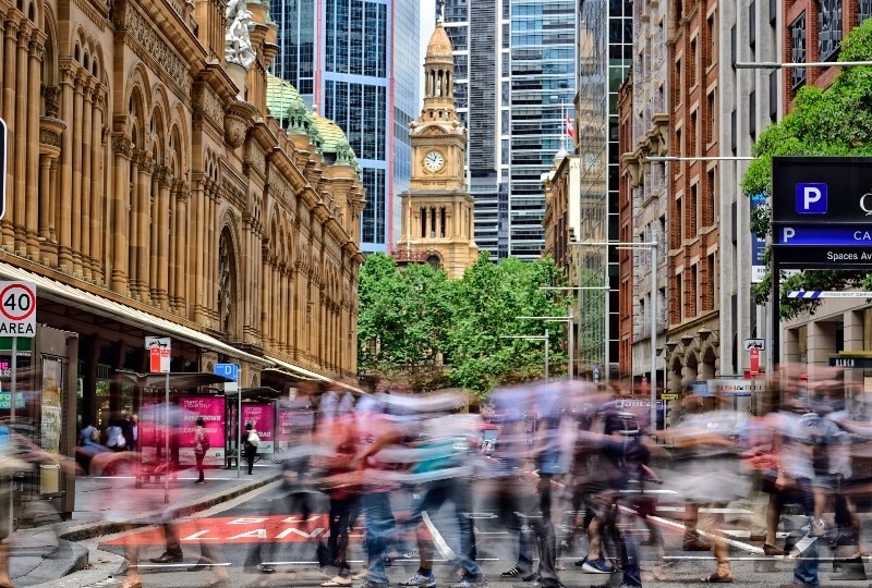 Crowds walking along George Street with heritage architecture and Sydney Town Hall in the background.