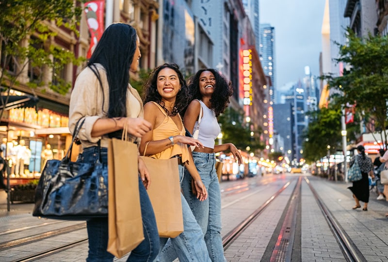 Friends walking and laughing with shopping bags along a Sydney city street at dusk.