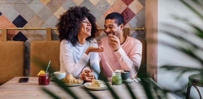 a couple laughing together in a restaurant booth as they share pastries and other refreshments
