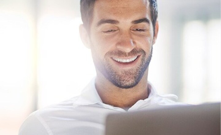  Happy bearded man in a bright room smiling at his laptop screen