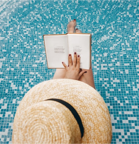 A person sitting on the edge of a pool reading a book