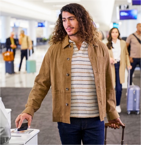 A person with long curly hair and a brown jacket holding a suitcase