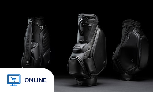 Three premium black golf bags by the brand Vessel are showcased in a dramatic, low-key studio setting. The bags are arranged in a trio, with the center bag facing forward and the two flanking bags angled to display their side profiles and carrying straps. Each bag is crafted from sleek, matte black synthetic leather with high-gloss accents, featuring waterproof zippers, padded straps, and the subtle "V" logo. The composition uses stark lighting against a deep black background to highlight the structural contours and luxurious textures of the bags, conveying an image of professional-grade quality and modern elegance. Online only.