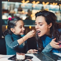 Young girl smiling while feeding cheesecake to her mum in a restaurant
