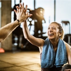 Woman in her 30s laughing while giving a high five to a trainer in the gym