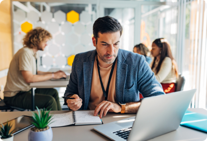 Man looking at laptop in an office making notes