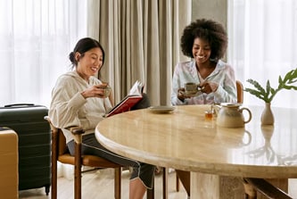Travel rewarding image alt text: Two women chatting and reading with cups of tea