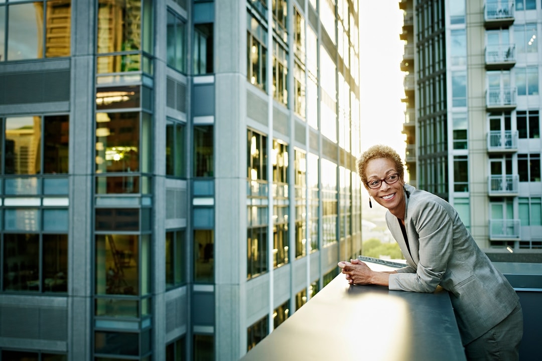 Woman standing on a balcony, looking out over a city of office buildings