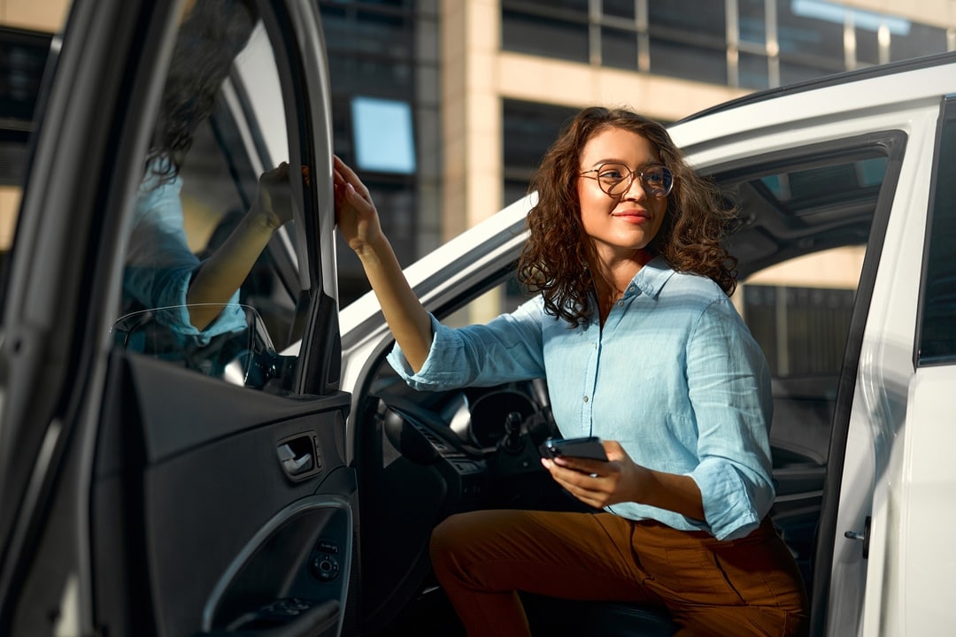 Woman stepping out of a car and holding a smartphone outside an office building