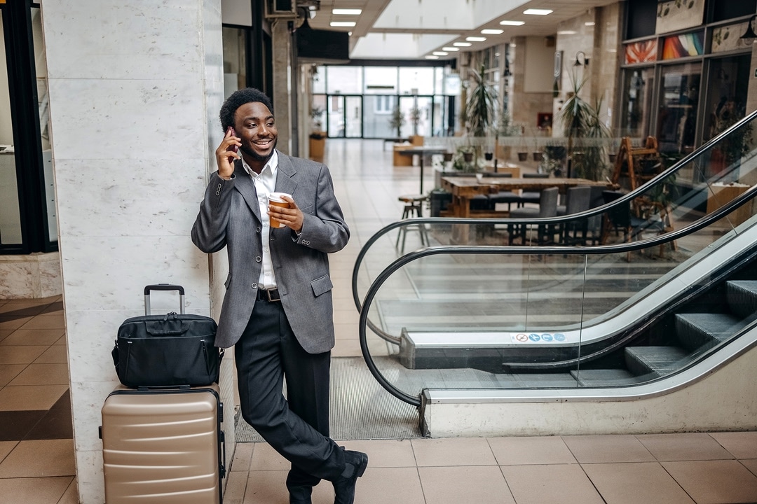 Man with a suitcase talking on a phone and holding a takeaway coffee in a terminal