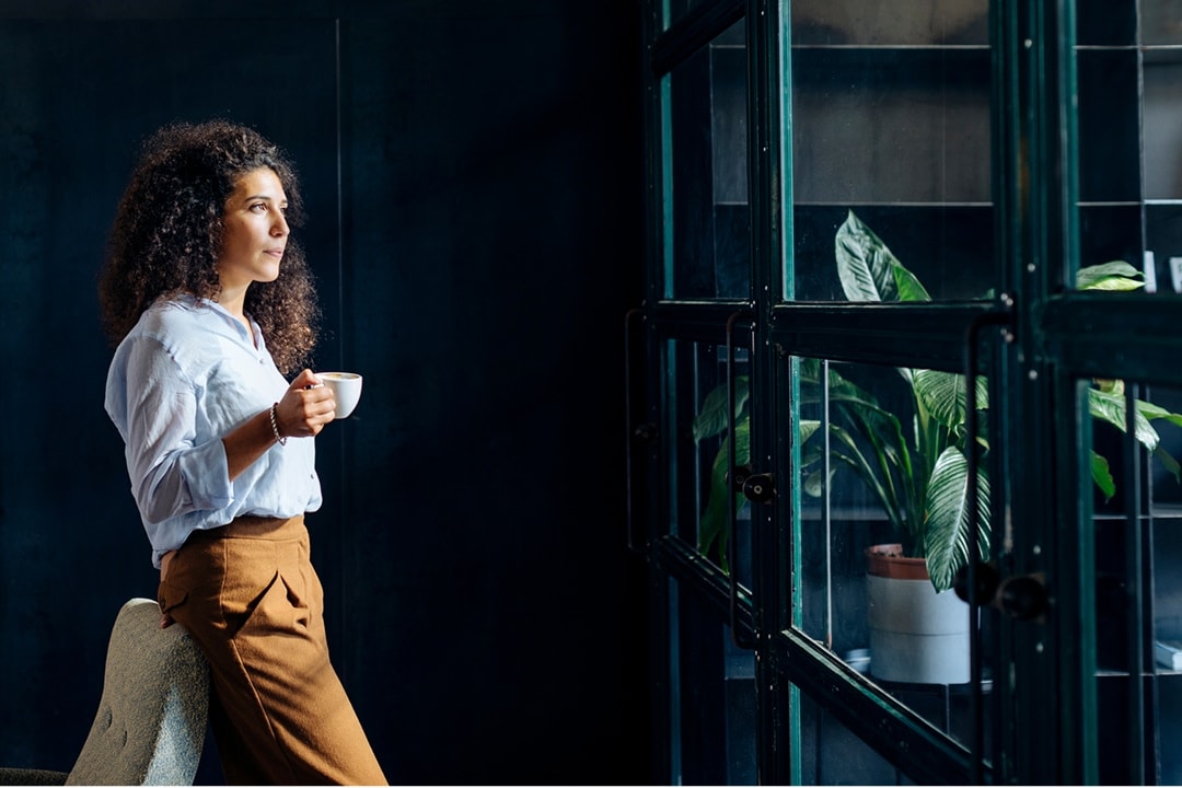 Woman standing by a window holding a cup of coffee