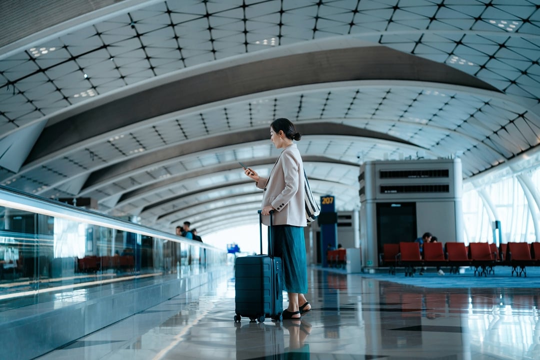 Woman standing in an airport terminal with a suitcase, looking at her phone