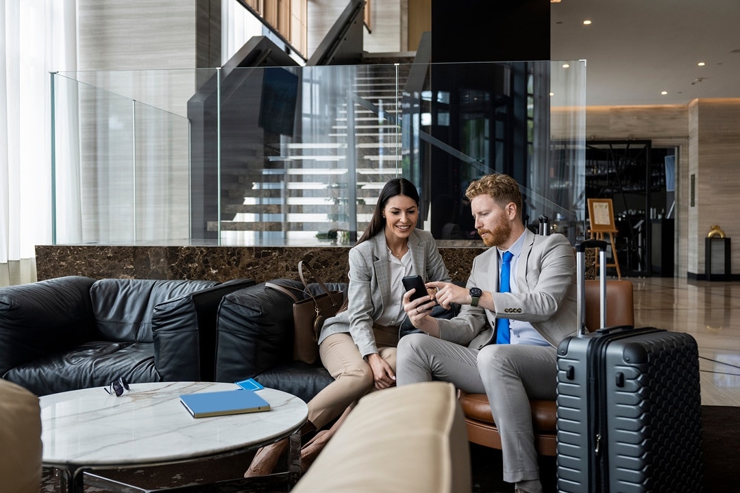 Two professionals sitting in a lounge with luggage, looking at a smartphone