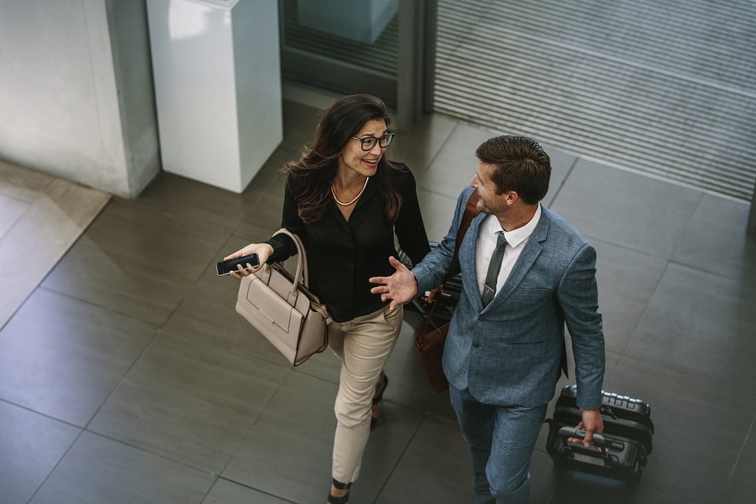 Two professionals walking with luggage, talking and smiling