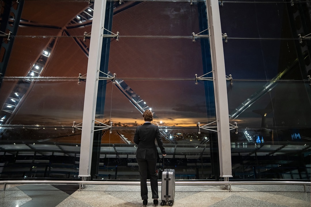 Professional standing by a window in an airport with a suitcase