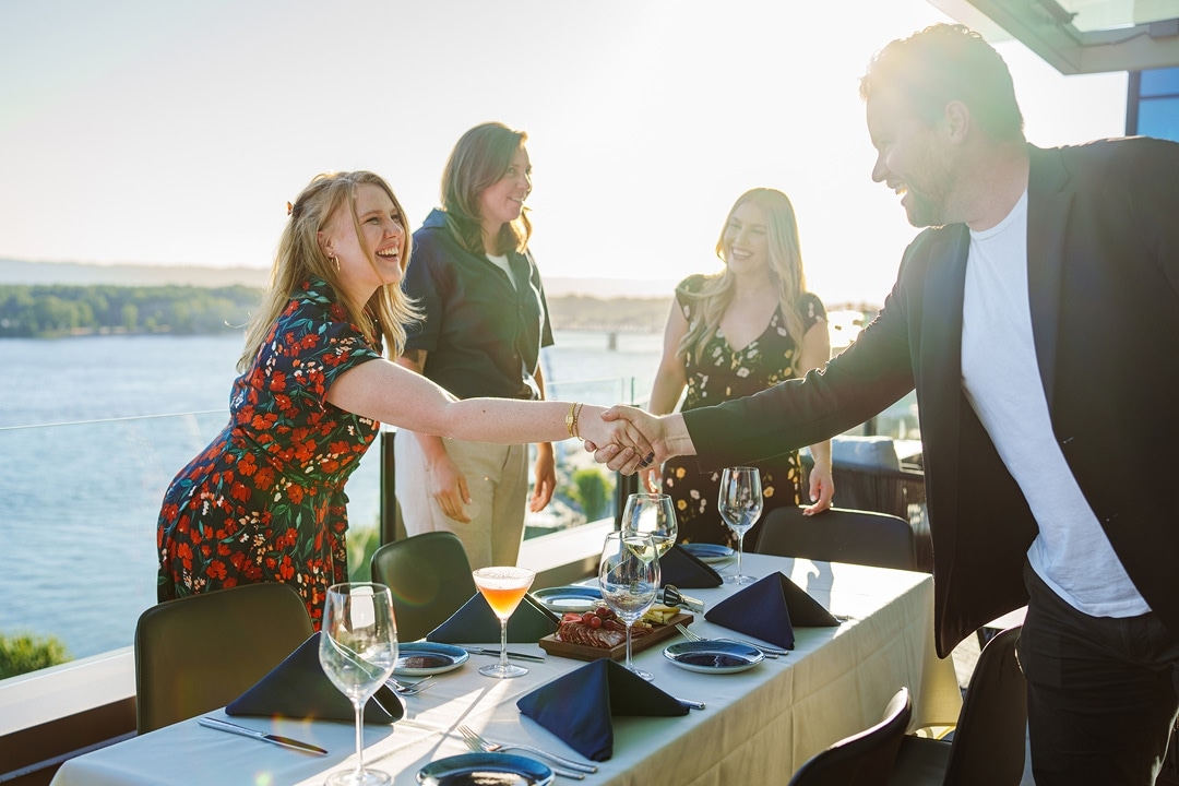 Group of people meeting and shaking hands at a restaurant terrace overlooking water